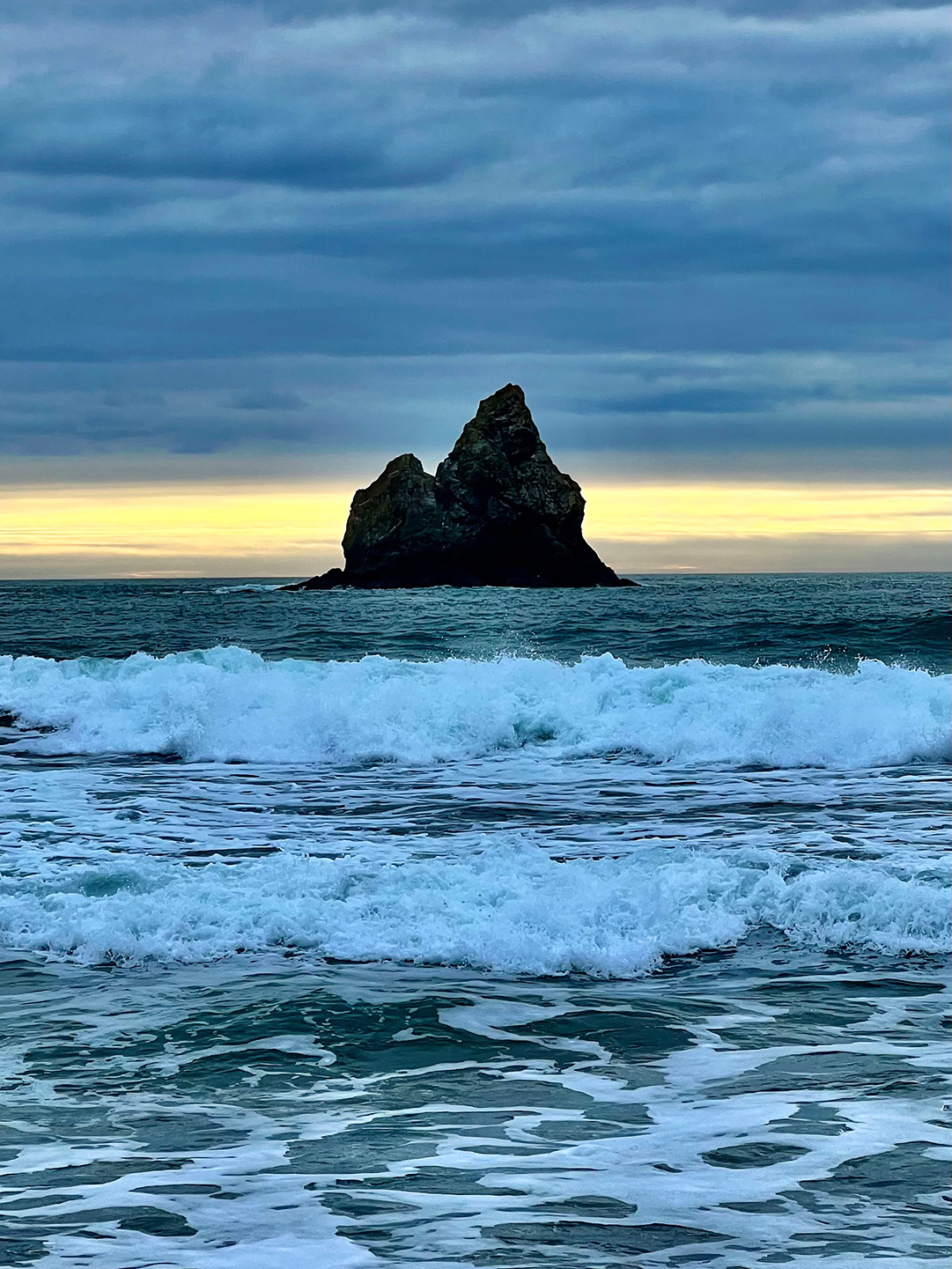 Rock formation in the ocean at sunset with foaming waves in the foreground.