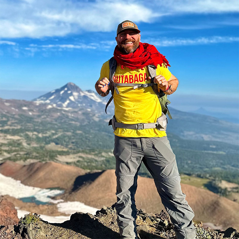 smiling Josh Rizzo posing on hike with mountain in the background